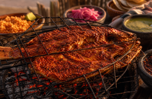 Huachinango zarandeado abierto en mariposa sobre una parrilla de carbón con arroz rojo y salsas mexicanas.