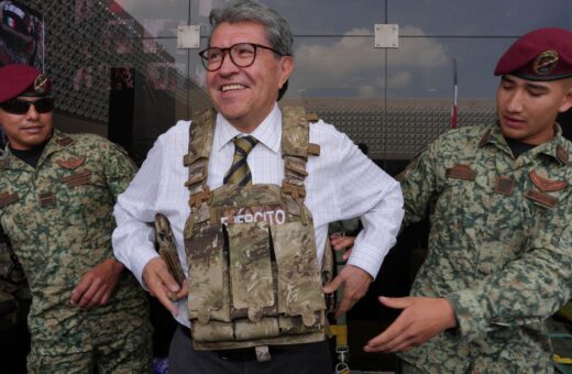 Ricardo Monreal prueba un chaleco táctico acompañado de dos militares durante una exhibición.