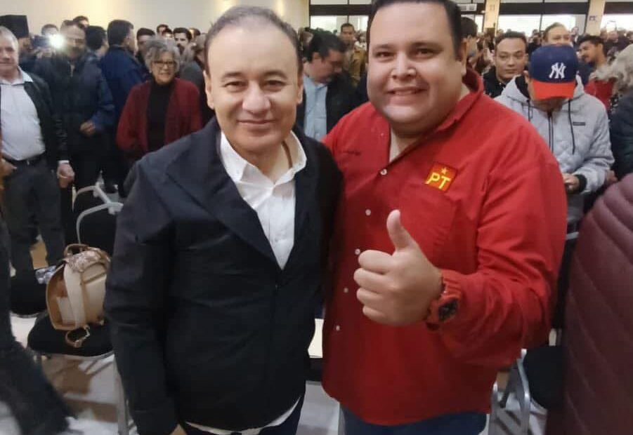Dos asistentes posan durante un encuentro político en Hermosillo; uno viste una camisa roja con el emblema del PT