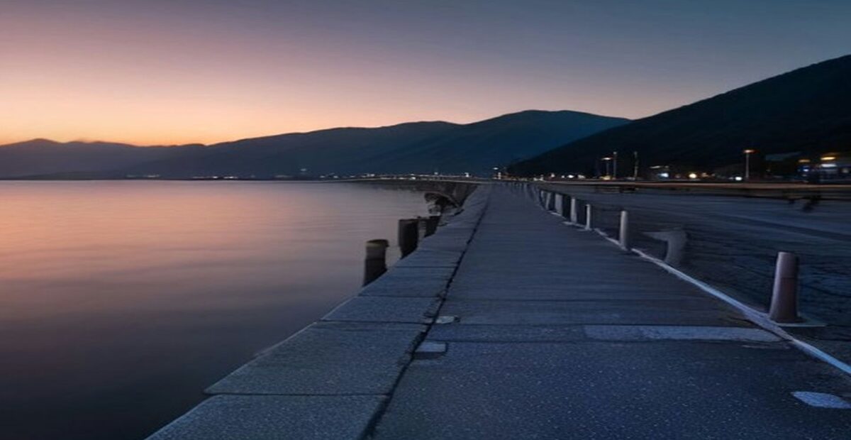 Muelle de concreto vacío con bolardos de amarre que se adentra en una bahía tranquila al atardecer
