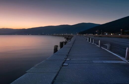Muelle de concreto vacío con bolardos de amarre que se adentra en una bahía tranquila al atardecer